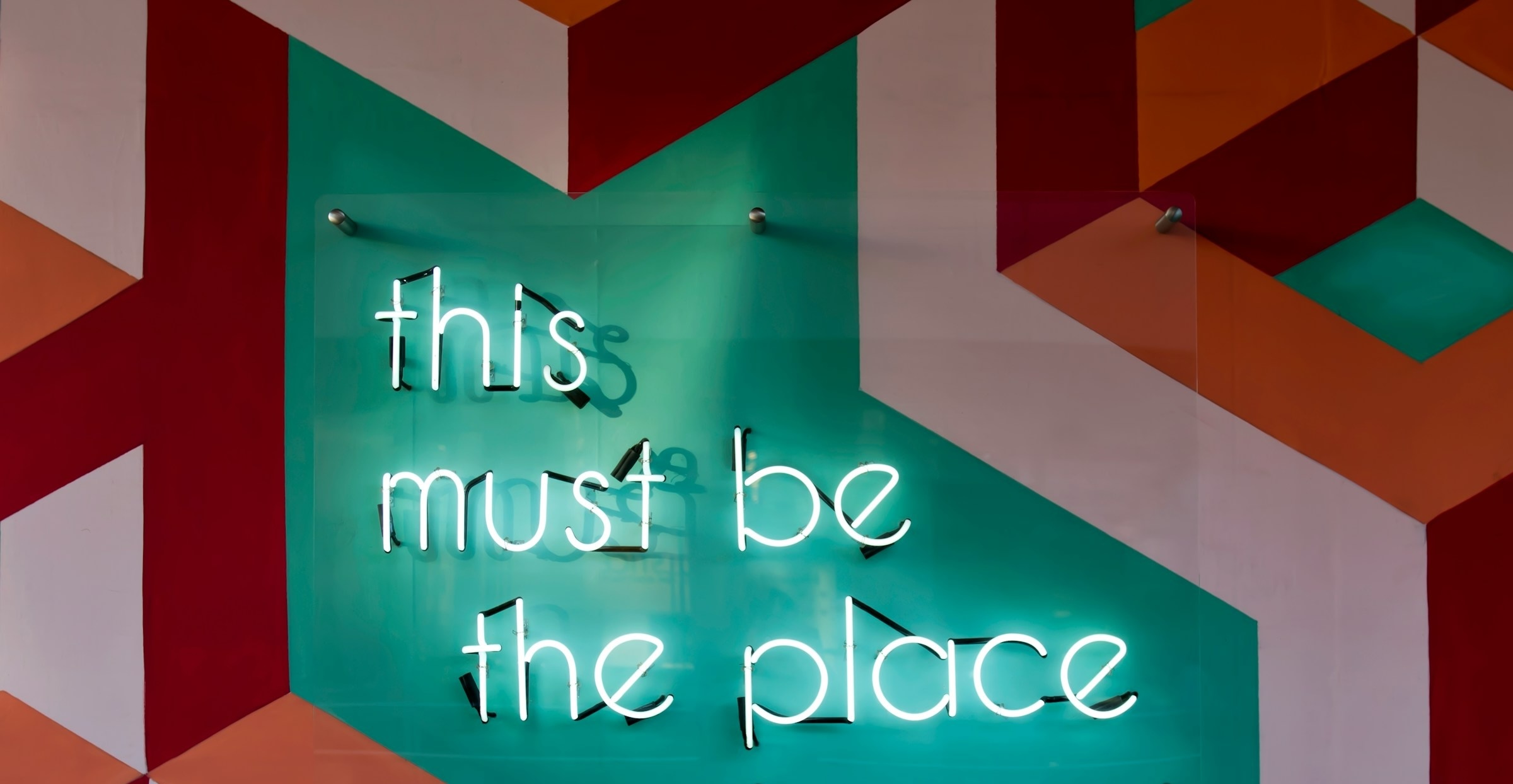 Modern office wall with colorful geometric patterns and 'this must be the place' neon text